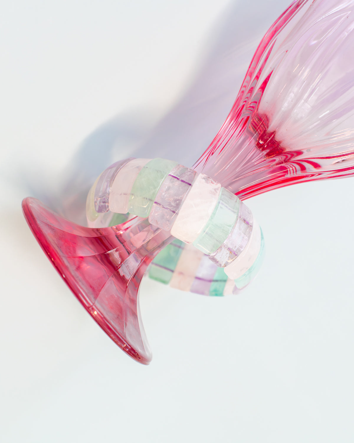 Close-up of a fluorite beaded bracelet draped over a pink glass vase, showing its translucent green, purple, and white striped beads.