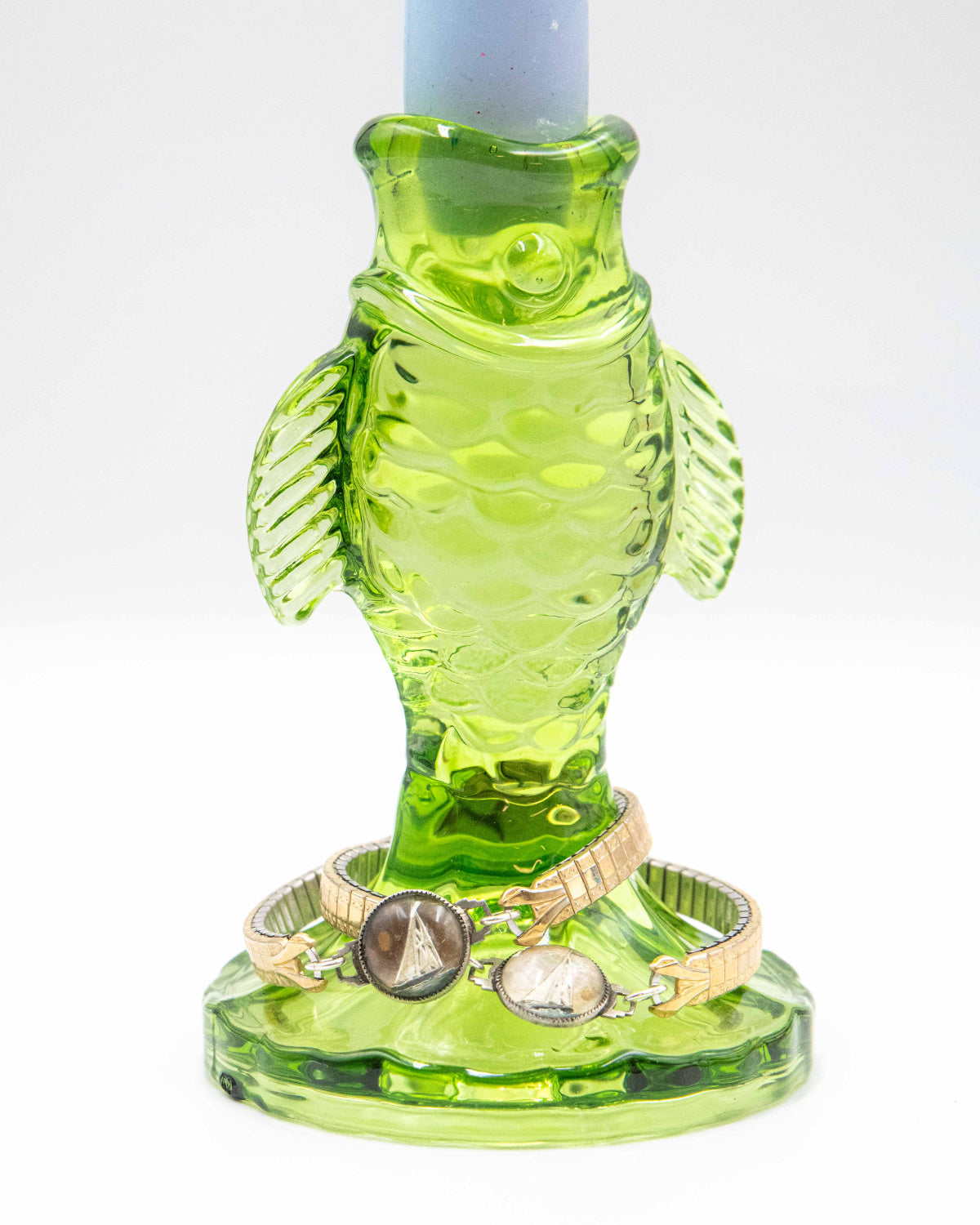 Green glass fish-shaped candle holder holding vintage bracelets with hand-painted glass pendants on a white background