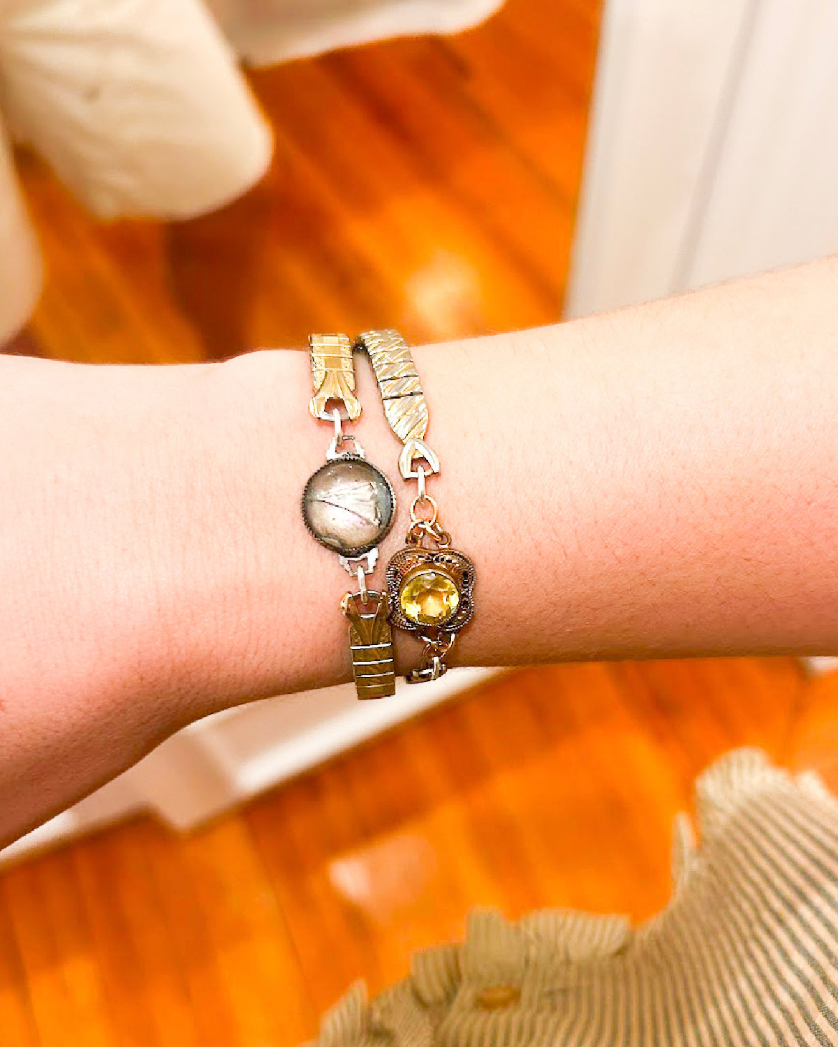 Close-up of a wrist wearing two gold bracelets with decorative elements on a blurred background.