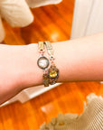 Close-up of a wrist wearing two gold bracelets with decorative elements on a blurred background.
