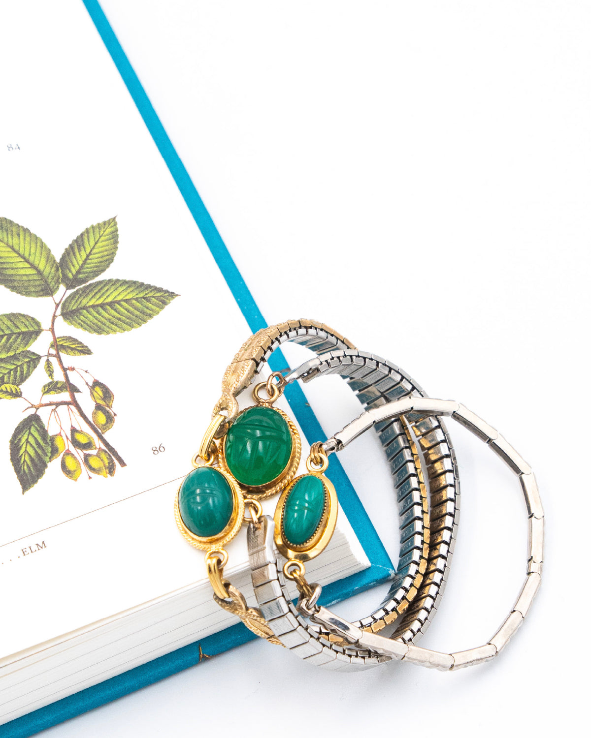 Three green scarab watch band bracelets on a white surface with a blue ribbon and leaf design.