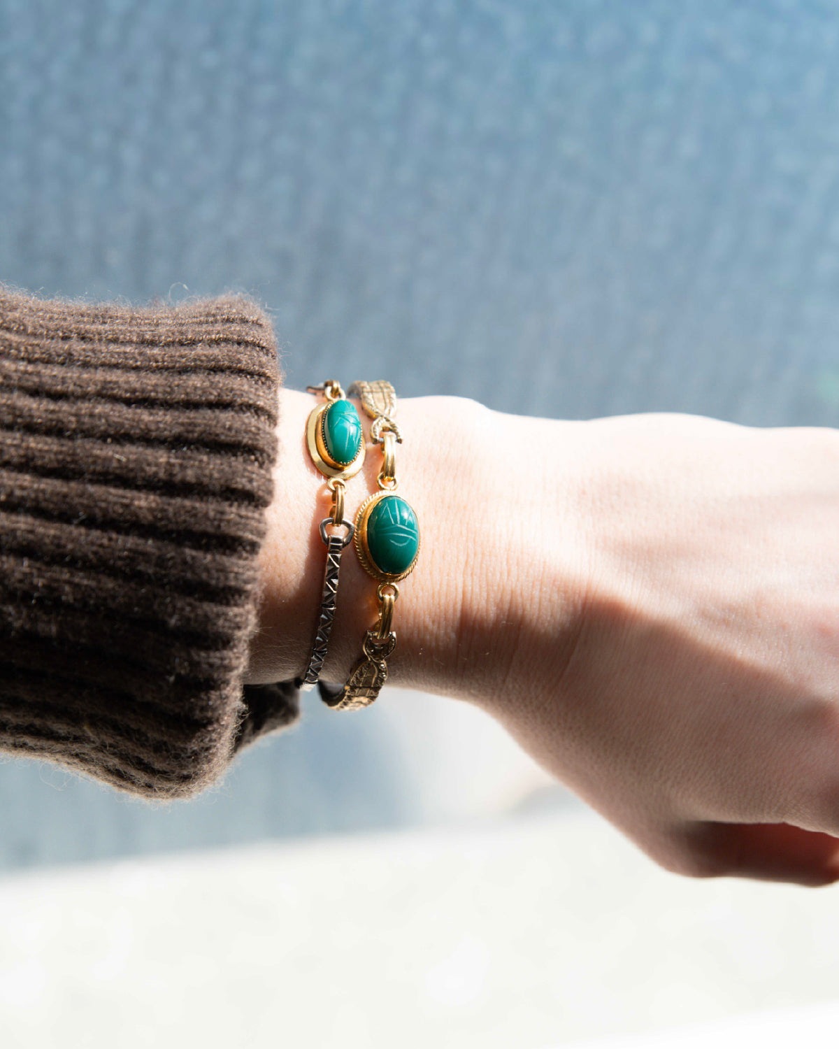 Bracelet with green scarab gemstones on a wrist against a neutral background
