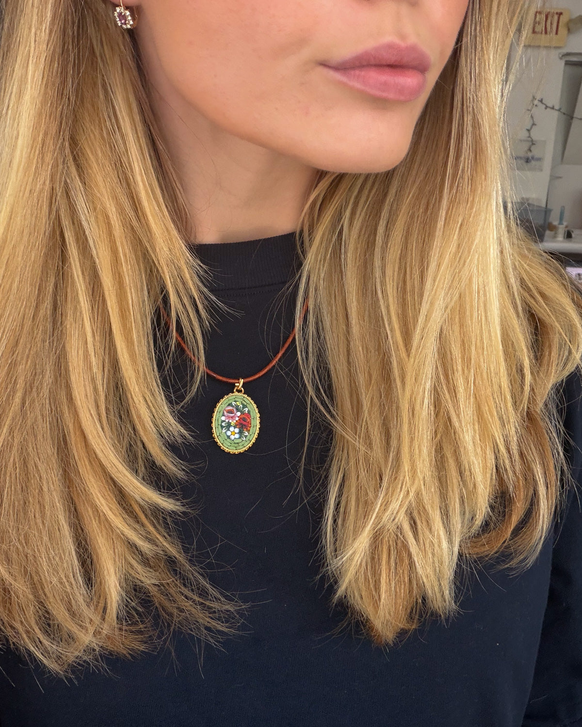 A close-up lifestyle shot of a woman with blonde hair wearing a colorful oval micro mosaic pendant necklace on a red cord, paired with a black top.