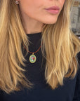 A close-up lifestyle shot of a woman with blonde hair wearing a colorful oval micro mosaic pendant necklace on a red cord, paired with a black top.