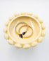 Yellow ceramic dish with decorative edge holding gold bracelets with deep purple goldstones on a white background