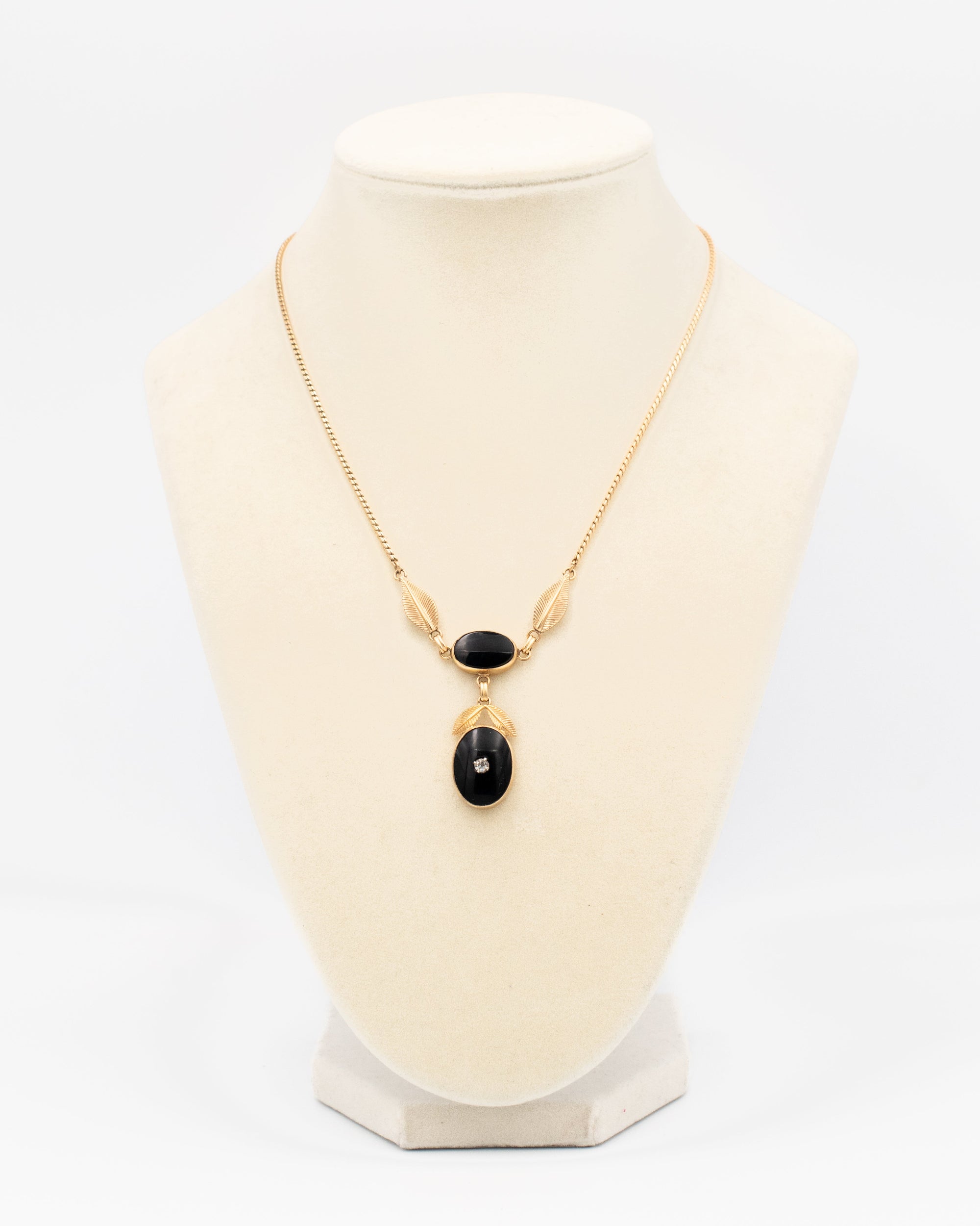 A gold chain necklace with a pendant featuring two black oval onyx stones and one larger black onyx teardrop stone, displayed on a cream-colored jewelry bust against a white background.