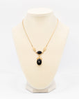 A gold chain necklace with a pendant featuring two black oval onyx stones and one larger black onyx teardrop stone, displayed on a cream-colored jewelry bust against a white background.
