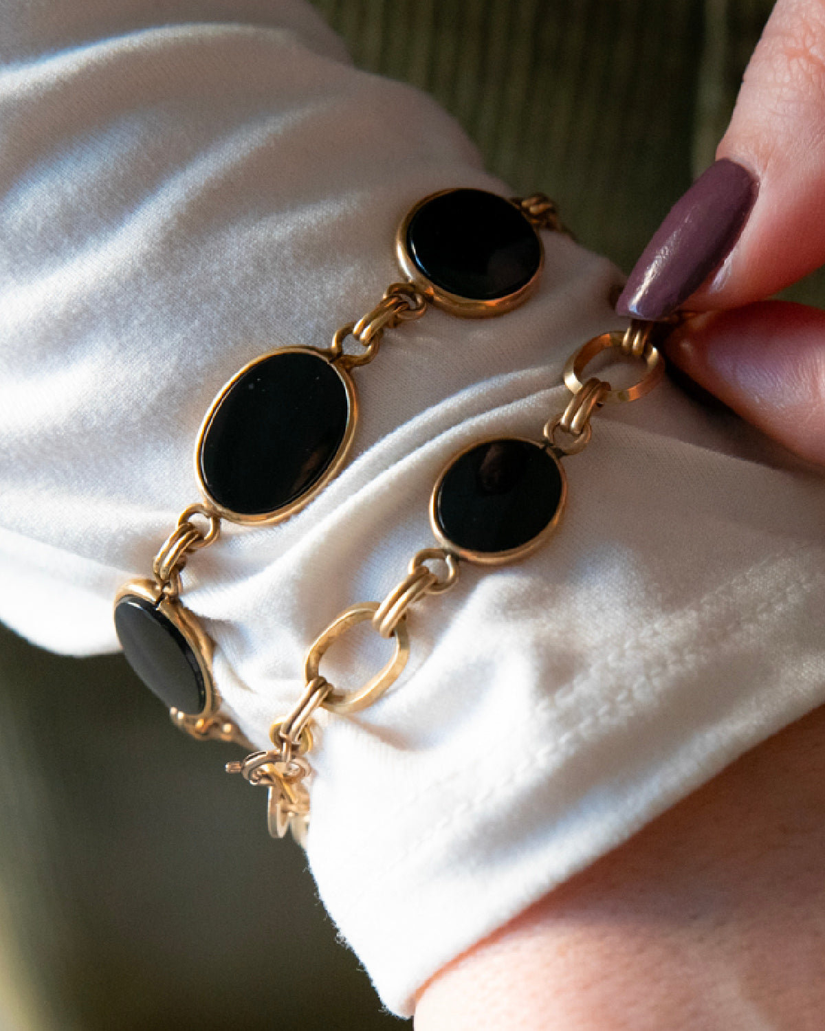 Detailed close-up of two vintage gold-filled bracelets with black onyx cabochons worn on a wrist.