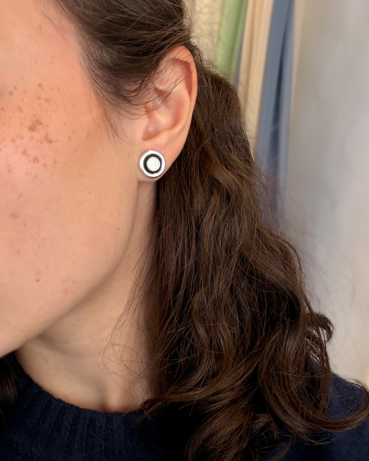 Close-up of a woman wearing round vintage opal earring studs with black and silver rims on a white background.