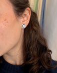 Close-up of a woman wearing round vintage opal earring studs with black and silver rims on a white background.