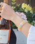 Woman wearing a pastel rainbow agate beaded bracelet in pink, yellow, and green tones while holding a bottle of rosé outdoors.