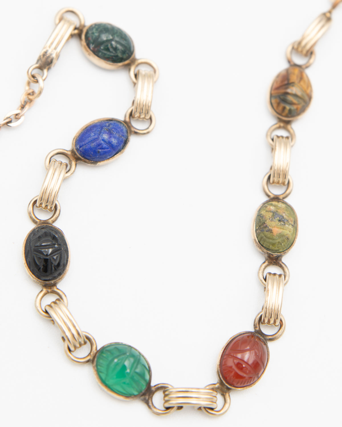 A gold-tone chain necklace featuring multiple oval cabochon scarab gemstones in green, blue, black, green, red, and brown, arranged on a plain white background.
