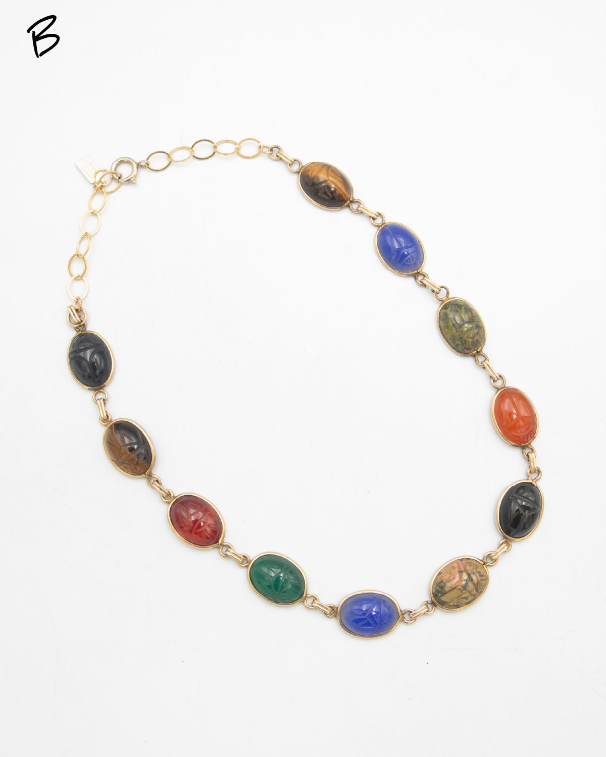 Vintage gold-filled necklace featuring multiple oval cabochon scarab gemstones carved with scarab beetle motifs in various colors including green, blue, brown, black, and red, set in gold links on a white background.