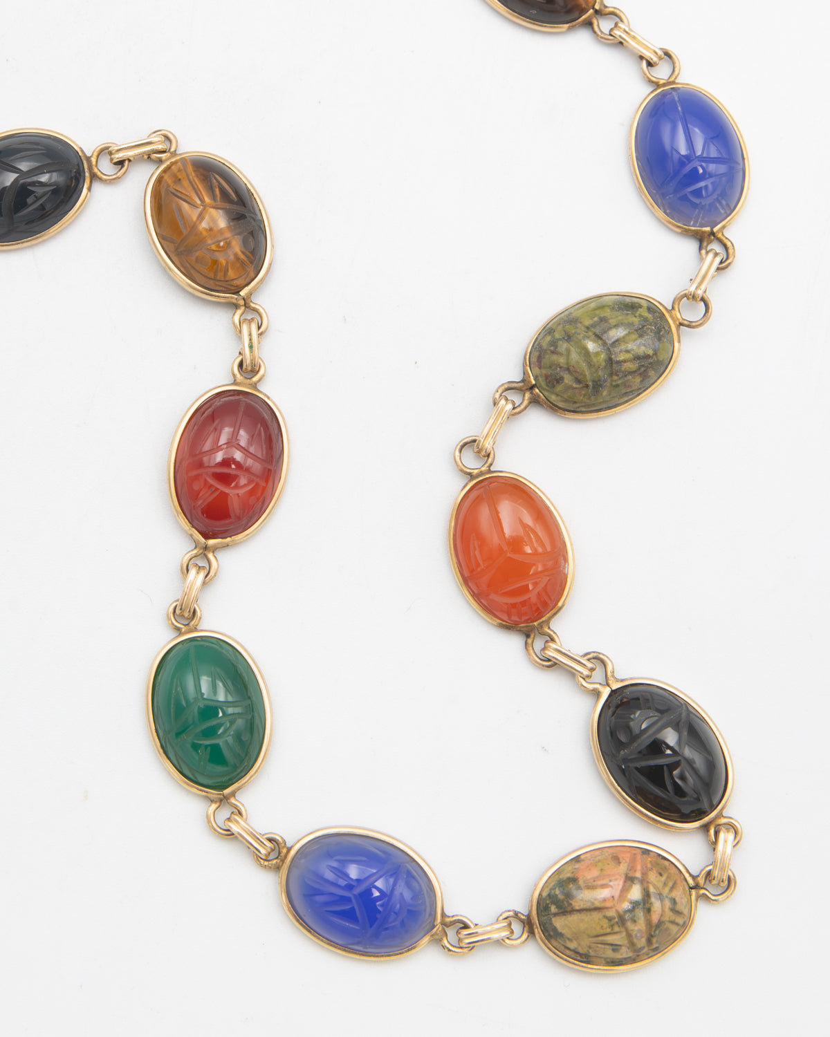 A gold-tone chain necklace featuring multiple oval cabochon gemstones in various colors including blue, green, red, orange, black, and brown, each carved with a scarab beetle motif.