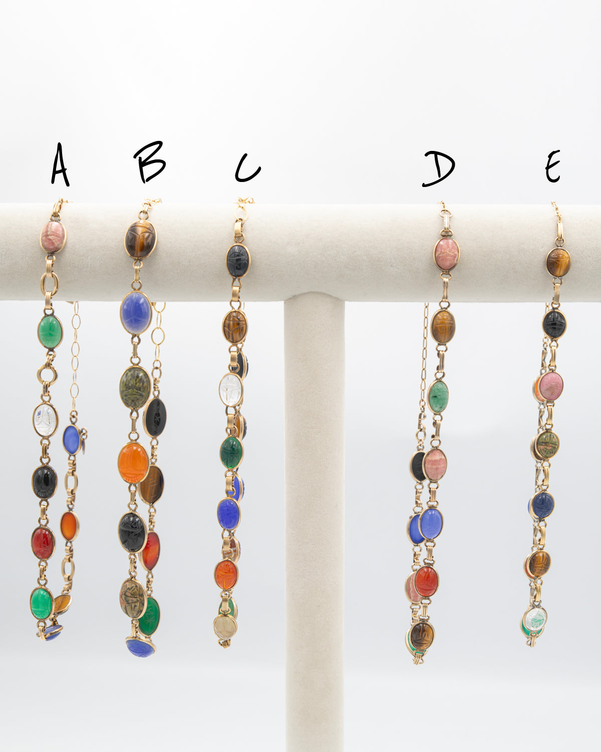 Five pairs of dangling beaded earrings displayed on a white jewelry stand, labeled A through E. The earrings feature multiple colorful round beads in green, blue, orange, pink, brown, black, and clear, suspended from gold-tone chains.