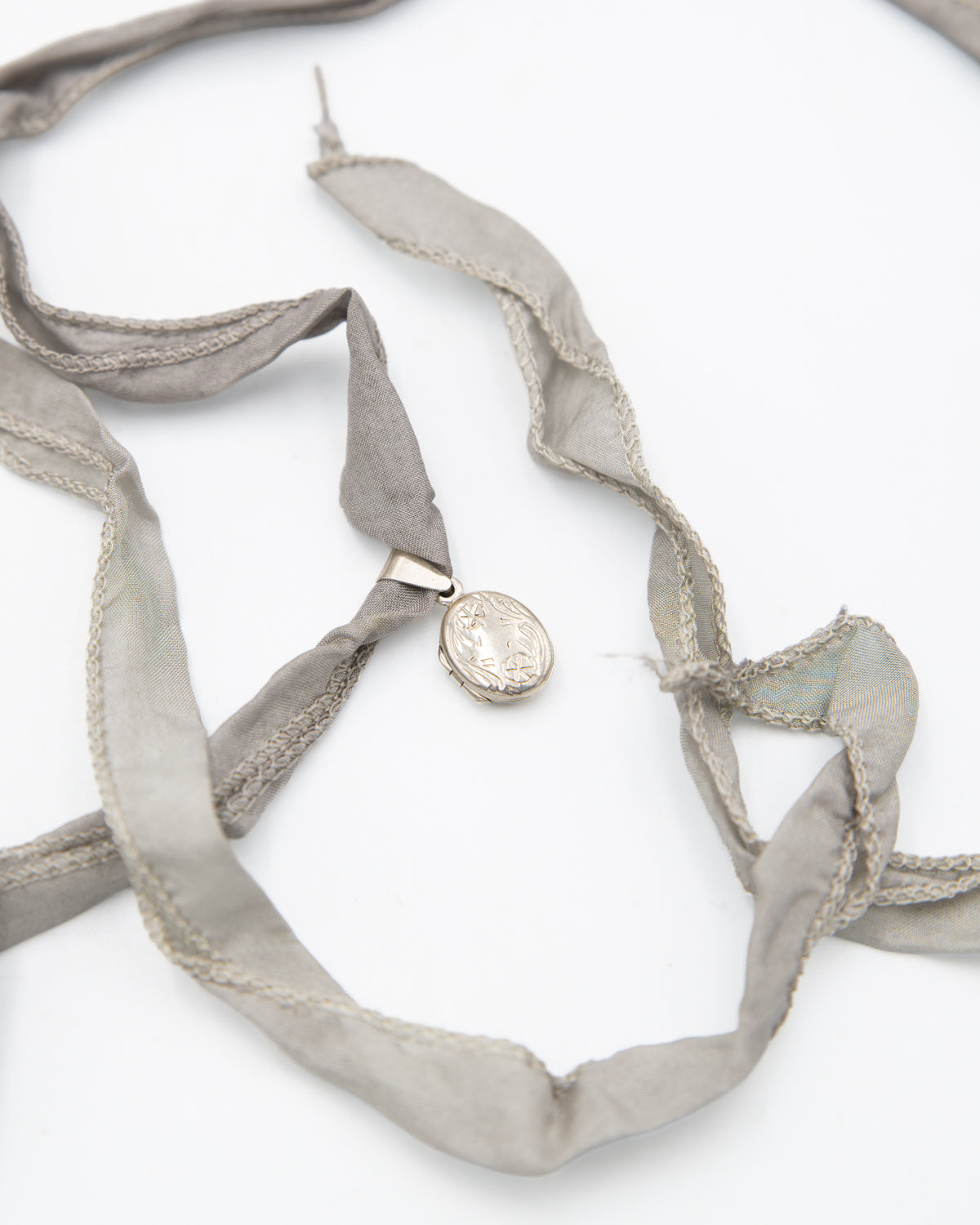 A sterling silver locket pendant necklace with a silver-toned metal clasp, attached to a wide, flowing light gray silk ribbon, photographed on a clean white background.