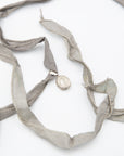 A sterling silver locket pendant necklace with a silver-toned metal clasp, attached to a wide, flowing light gray silk ribbon, photographed on a clean white background.