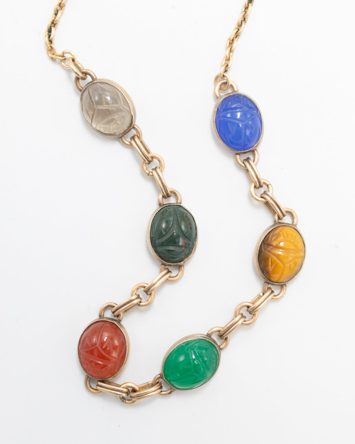 Close-up of two scarab gemstone necklace strands showing carved beetle details in clear, green, blue, red, and tiger's eye stones.