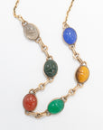 Close-up of two scarab gemstone necklace strands showing carved beetle details in clear, green, blue, red, and tiger's eye stones.