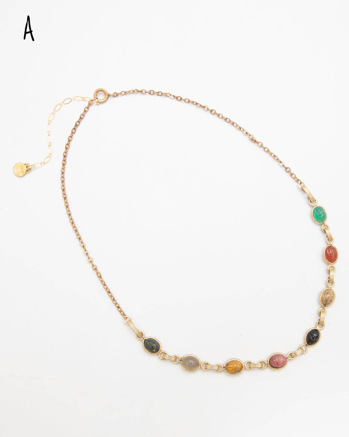 Scarab gemstone necklace with seven carved stone beetles in earthy and jewel tones, laid flat with its extender chain and charm visible.