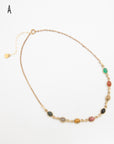 Scarab gemstone necklace with seven carved stone beetles in earthy and jewel tones, laid flat with its extender chain and charm visible.
