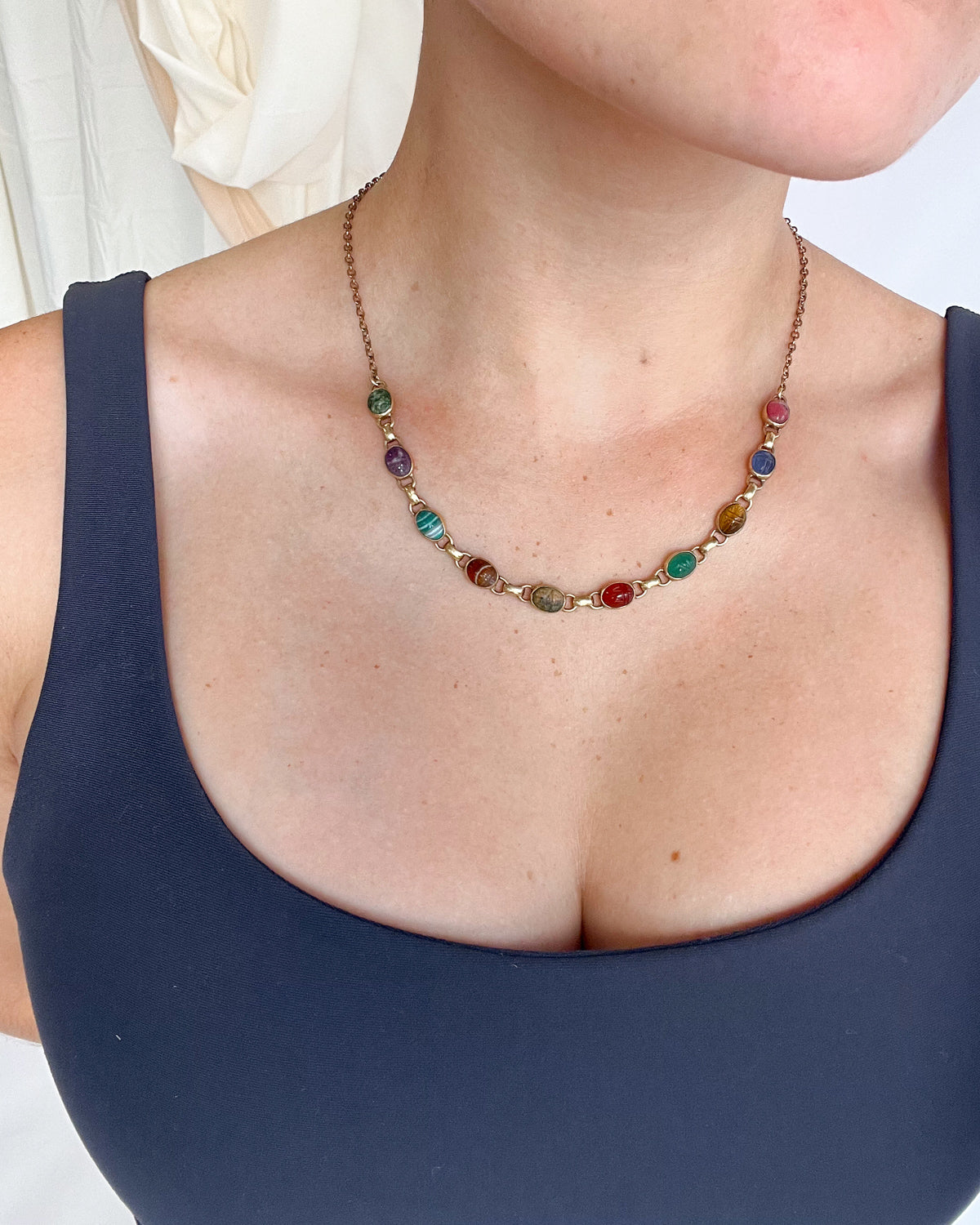 Close-up of a woman wearing a colorful scarab gemstone necklace layered against a navy top.