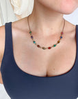 Close-up of a woman wearing a colorful scarab gemstone necklace layered against a navy top.