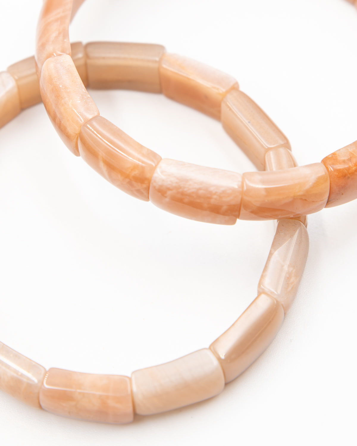 Close-up of two peach-toned sunstone beaded bracelets overlapping against a white background, highlighting their tumbled cylindrical beads.