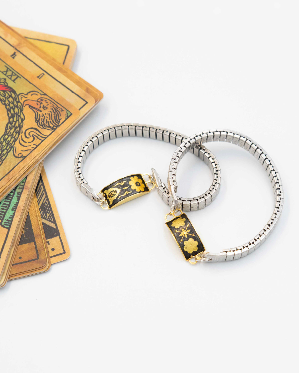 Vintage watch band bracelets featuring a curved Damascene panel, set on a stretch metal band reclaimed from vintage timepieces, on a white background and tarot cards