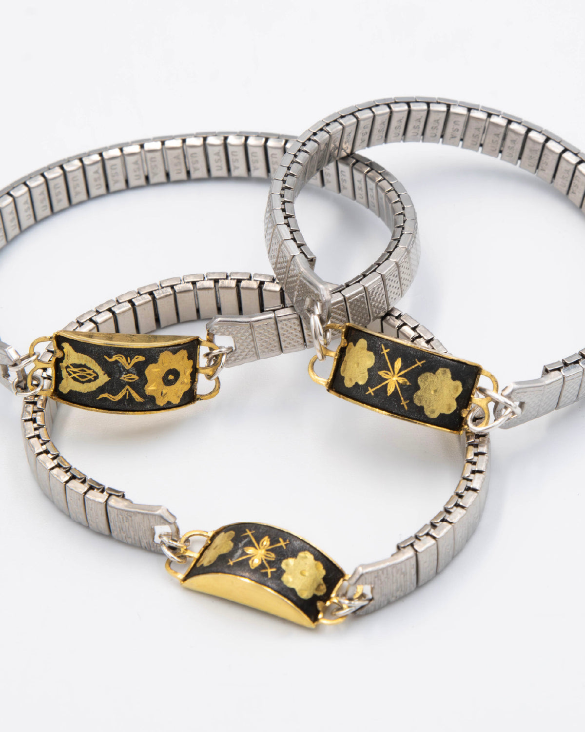 Silver bracelets with black and gold decorative elements on a white background