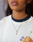 A close-up of a person wearing a delicate gold chain 19th century Victorian necklace with a small heart-shaped charm and a drop clasp, styled over a white ringer t-shirt with a navy collar.
