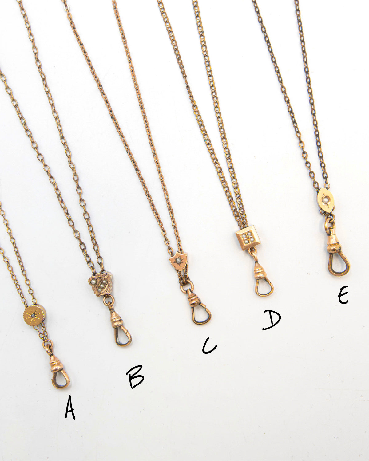 Five antique gold-filled chatelaine necklaces with dog clip clasp closures are arranged diagonally on a white background, labeled A through E.