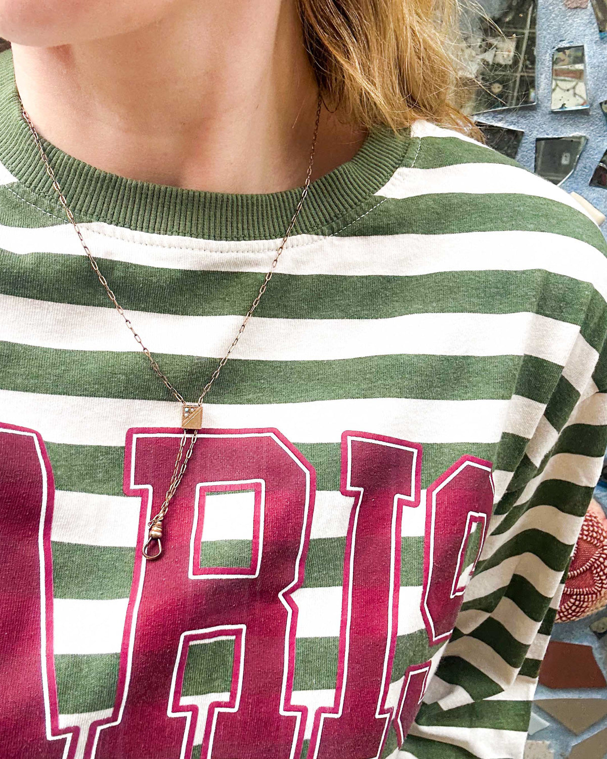 Person wearing a green and white striped shirt with a Victorian-era chatelaine slider necklace