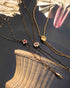 Three antique Victorian-era lariat chatelaine slider necklaces with decorative pendants arranged on a dark textured surface with a woven basket and dried flowers as props. The necklaces feature a star pendant with a red gem, a floral pendant with a red gem and clear stones, and a small gold heart pendant.