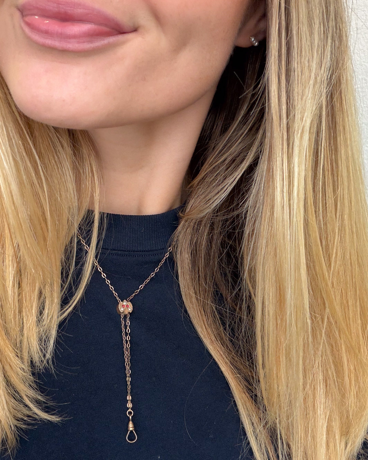 A close-up of a woman wearing a delicate rose gold lariat necklace with a small round bead and a dangling loop, paired with a dark navy top.