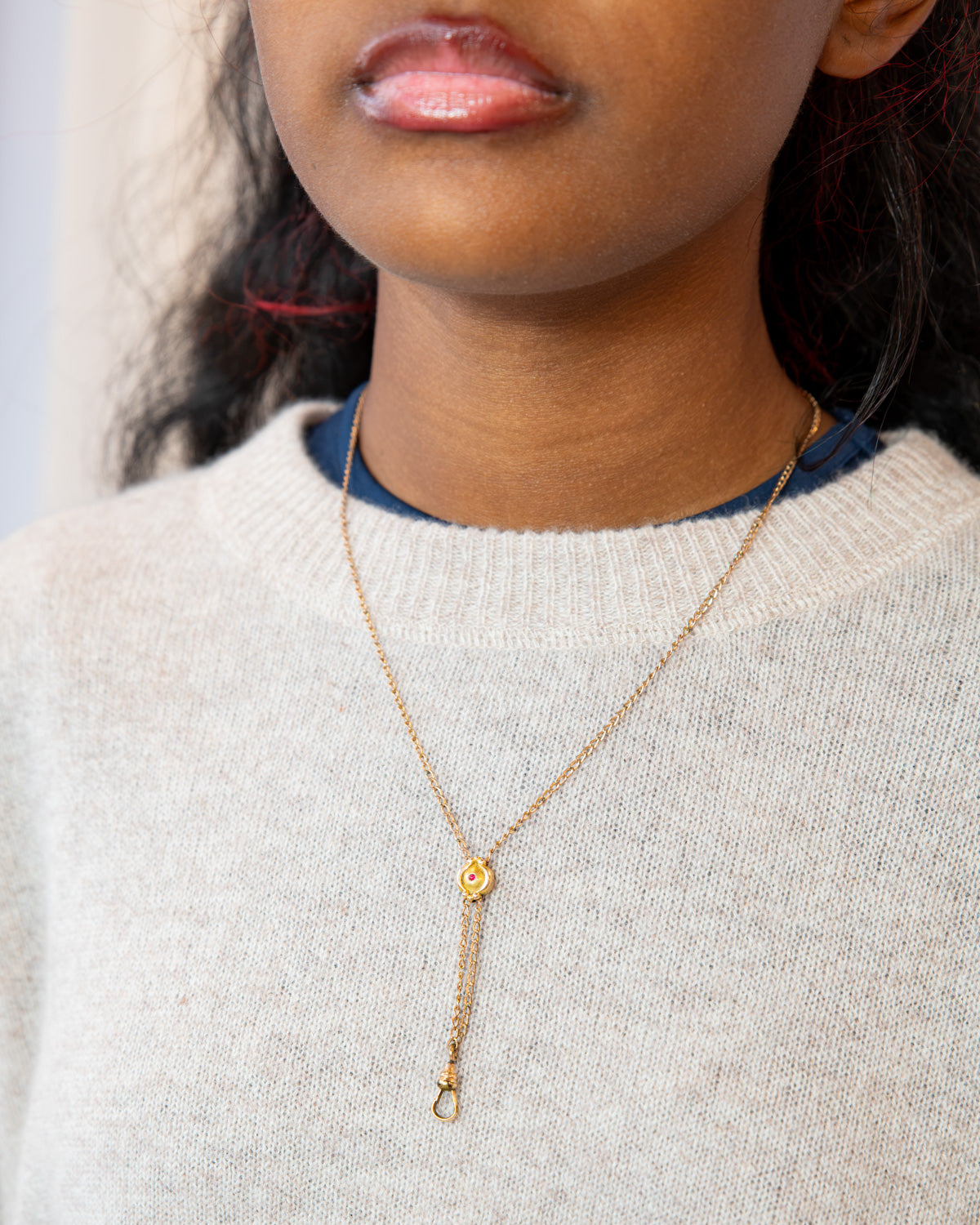 Woman wearing 19th century solid gold chatelaine slider necklace with an encrusted ruby glass stone. 