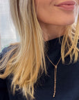 A close-up of a woman wearing a delicate gold lariat chatelaine necklace with a long drop chain and a small dangling charm, paired with a black top.