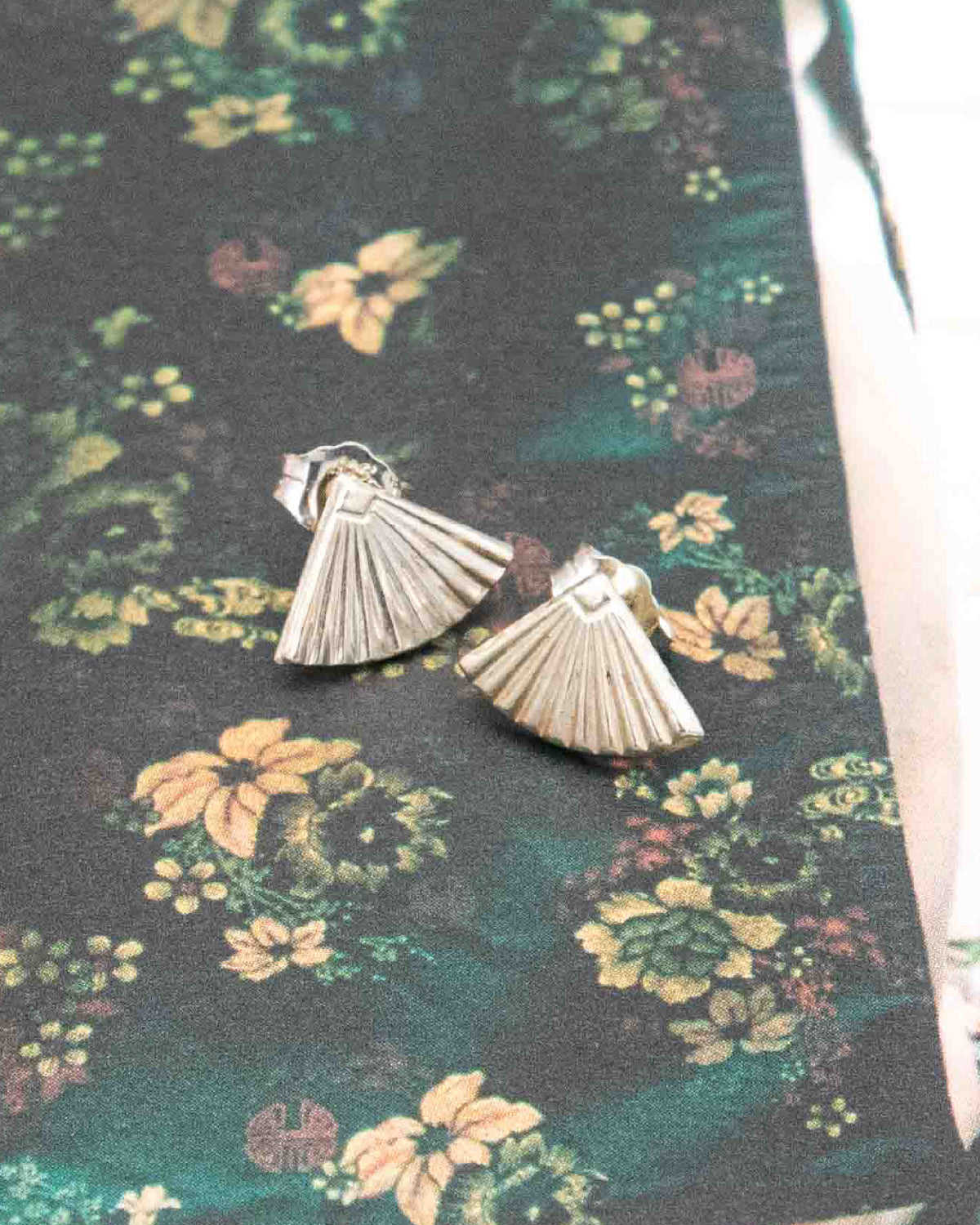 Silver fan-shaped earrings on a floral fabric background