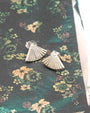Silver fan-shaped earrings on a floral fabric background