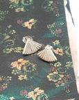 Silver fan-shaped earrings on a floral fabric background