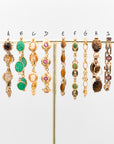 Collection of vintage gold-filled bracelets from the 1930s–1960s featuring cameos, carved stones, Peking glass, and gemstone cabochons displayed on a gold stand