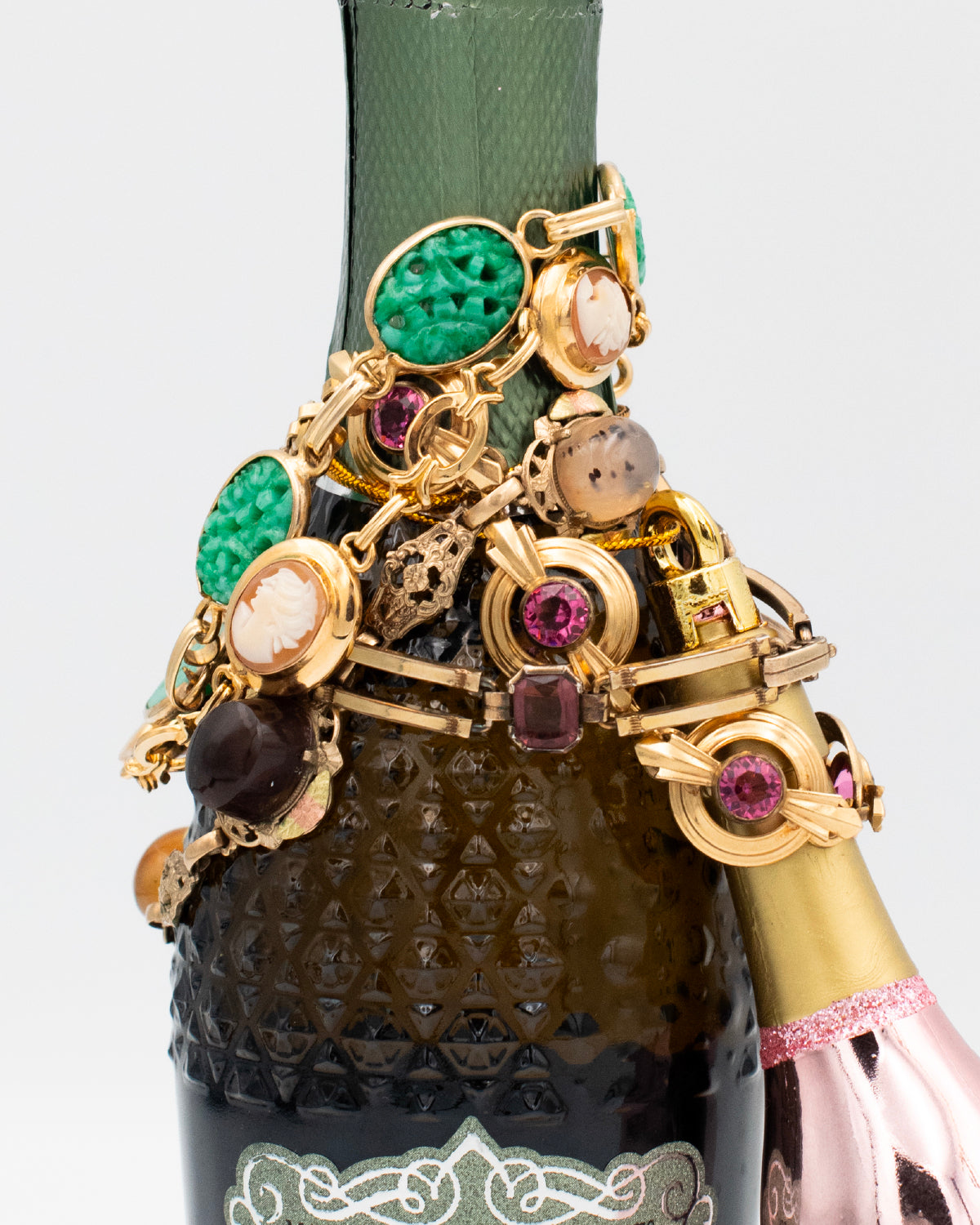 Vintage gold-filled bracelets with carved stones, cameos, and glass cabochons draped over Prosecco bottle for a styled product display