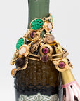Vintage gold-filled bracelets with carved stones, cameos, and glass cabochons draped over Prosecco bottle for a styled product display