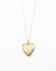 A gold heart-shaped locket pendant on a delicate gold chain, displayed against a clean white background.