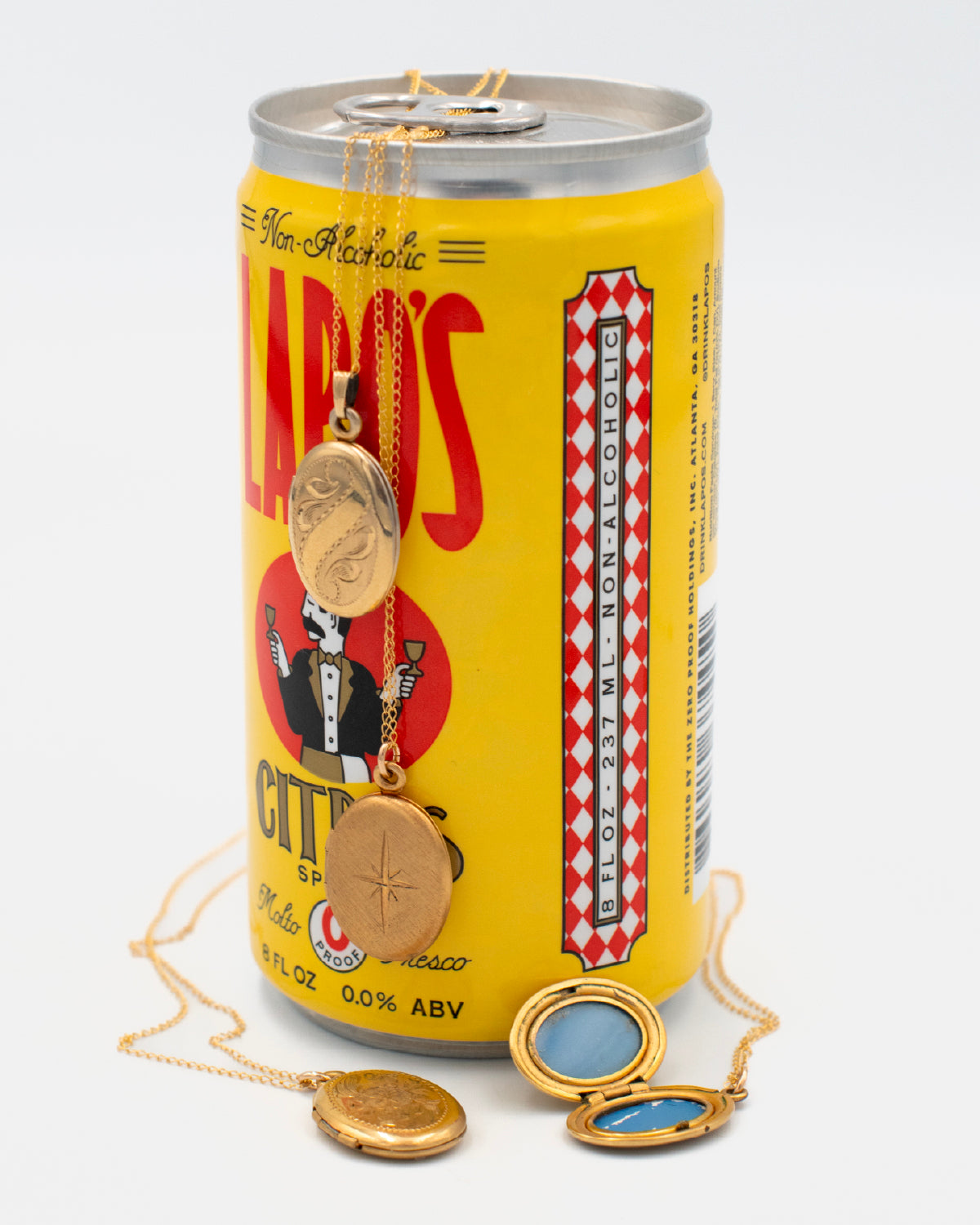 Two vintage, engraved oval lockets displayed on a yellow can, one is beside the can and another is besdie and open, revealing a blue interior lining