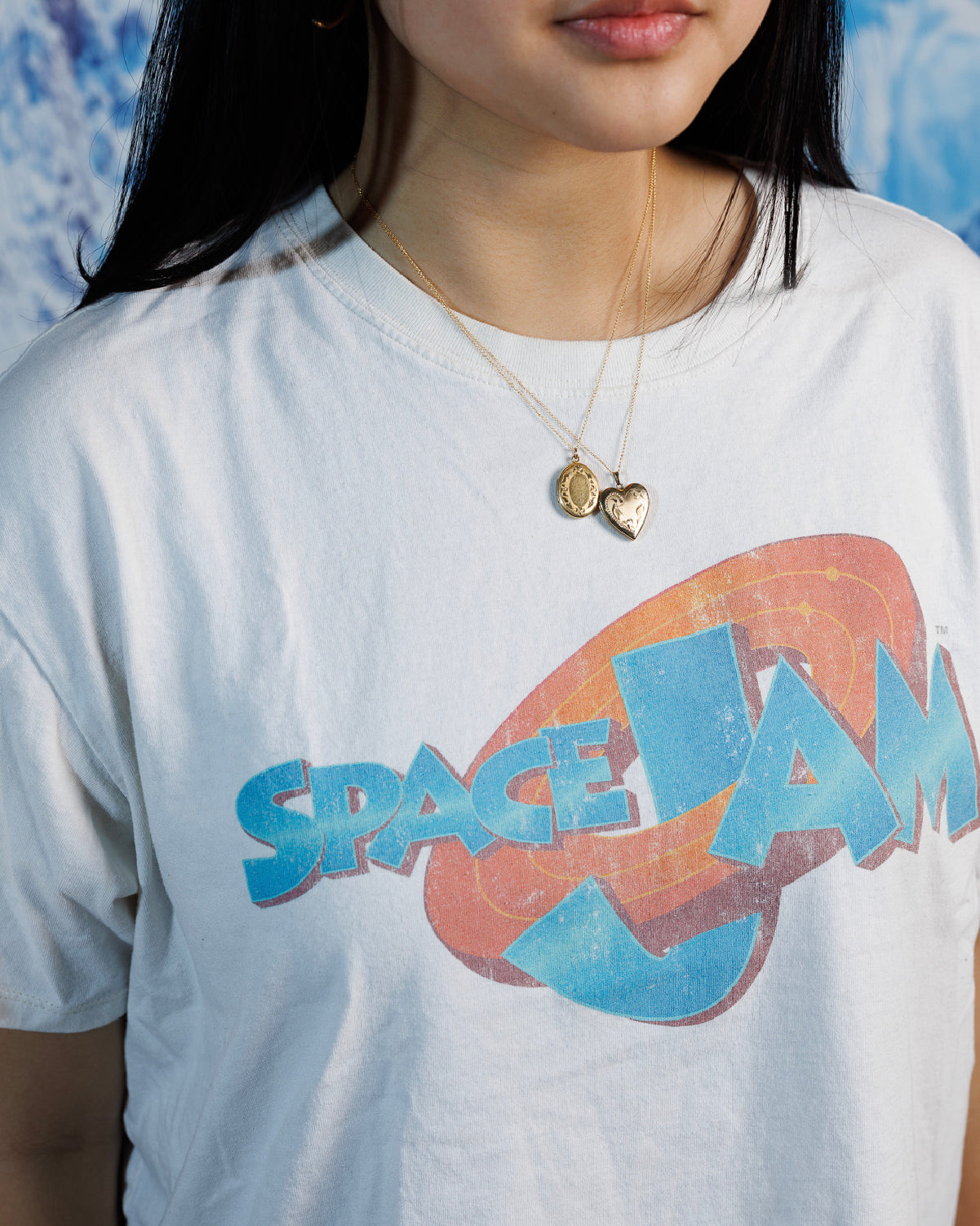 Woman wearing two engraved, vintage lockets (heart & oval) over a white graphic t-shrit. 