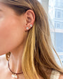 Close-up of a person wearing silver shell-shaped stud earrings with a blurred cityscape background
