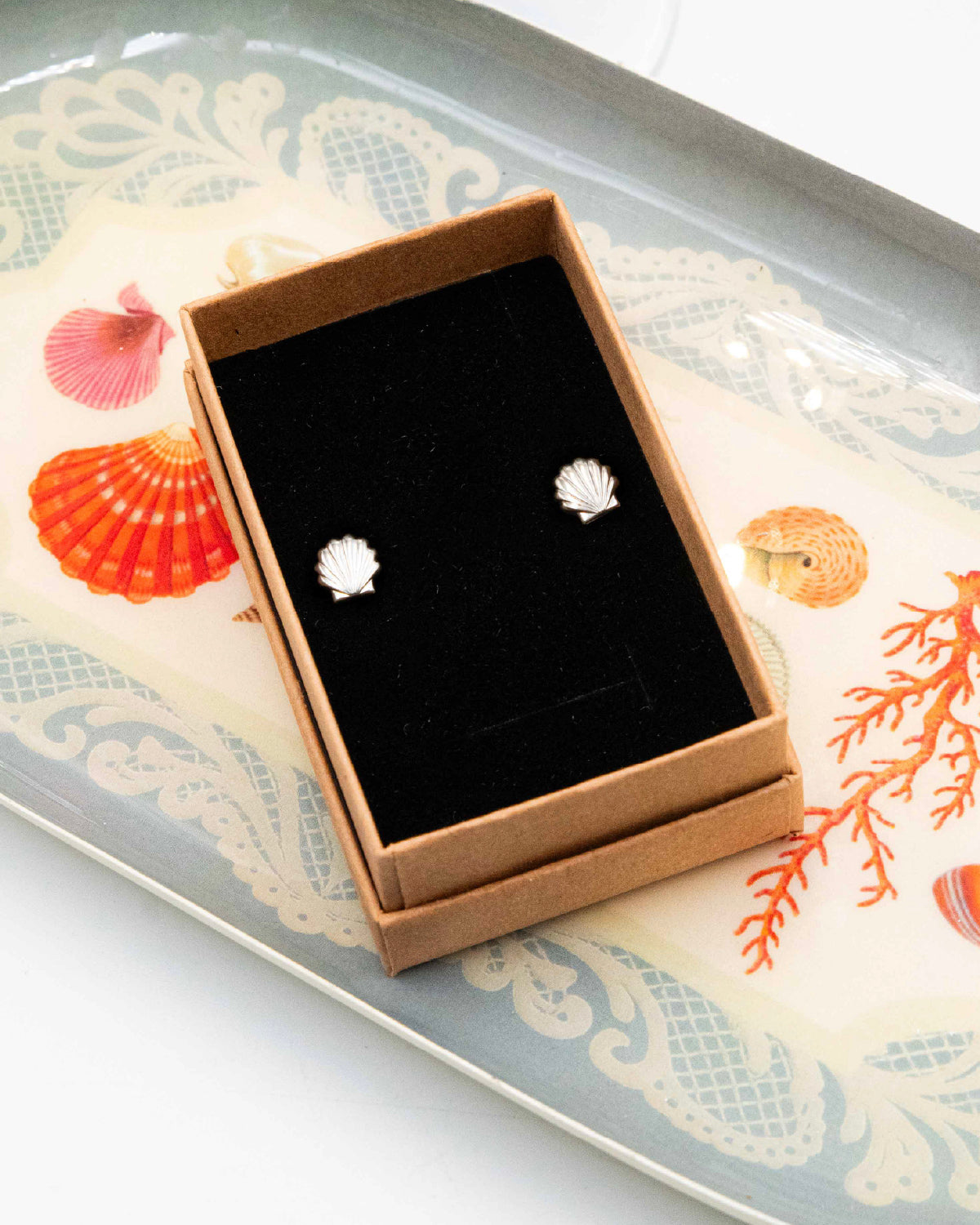 Shell-shaped earrings in a box on a decorative tray with seashell design