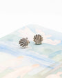 Silver shell-shaped earrings on a soft fabric background
