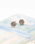 Silver shell-shaped earrings on a soft fabric background